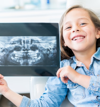 young, smiling girl holding up her dental x-ray